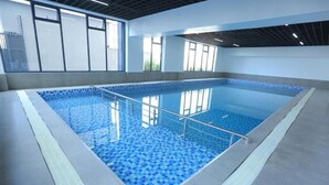 An indoor swimming pool with clear blue tiles, a metal safety railing, and large windows allowing natural light. - Lux Suites Perry West Luxurios Apartment (Nairobi)