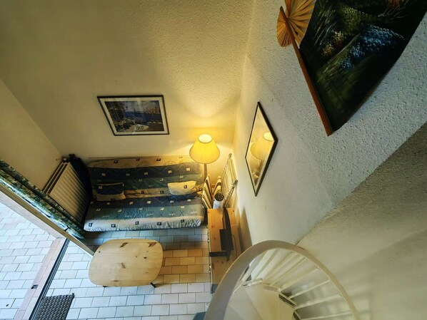 Un escalier menant à une chambre à coucher équipée d’un lit, d’une table de chevet et d’une lampe.