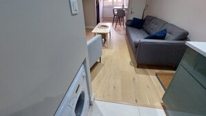 A compact living space with a grey sofa, a small wooden table, and a white radiator. - Modern Duplex Near Slopes, Ski Access (Les Deux Alpes)