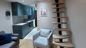 A modern apartment with a kitchen, a grey sofa, a white armchair, and a spiral staircase. - Modern Duplex Near Slopes, Ski Access (Les Deux Alpes)