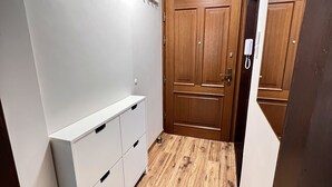 Un pasillo estrecho con suelo de madera, un armario blanco y una puerta de madera con un teléfono.