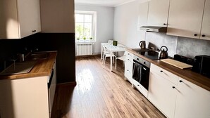 Una cocina moderna con piso de madera, armarios blancos, una mesa de comedor y una ventana que proporciona luz natural.