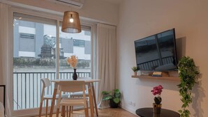 Ein modernes Wohnzimmer mit Essbereich, einem an der Wand befestigten Fernseher und einem Balkon mit Blick ins Freie.