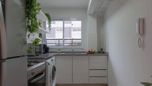 Eine kompakte Küche mit Einbauofen, Waschmaschine und Fenster mit Blick auf Gebäude.