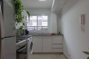 A compact kitchen with a built-in oven, a washing machine, and a window with a view of buildings.