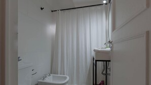 Ein kleines, weißes Badezimmer mit Duschvorhang, Waschbecken mit Spiegel und Toilette.
