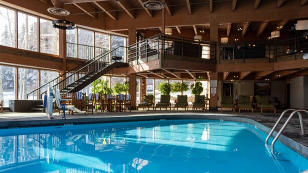 Une grande piscine intérieure avec un décor en bois, plusieurs niveaux dotés de balcons et des espaces extérieurs aménagés pour se détendre.