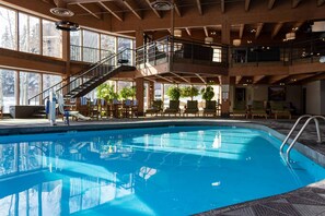 A large indoor swimming pool with a wooden interior, multiple levels with balconies, and outdoor seating areas.