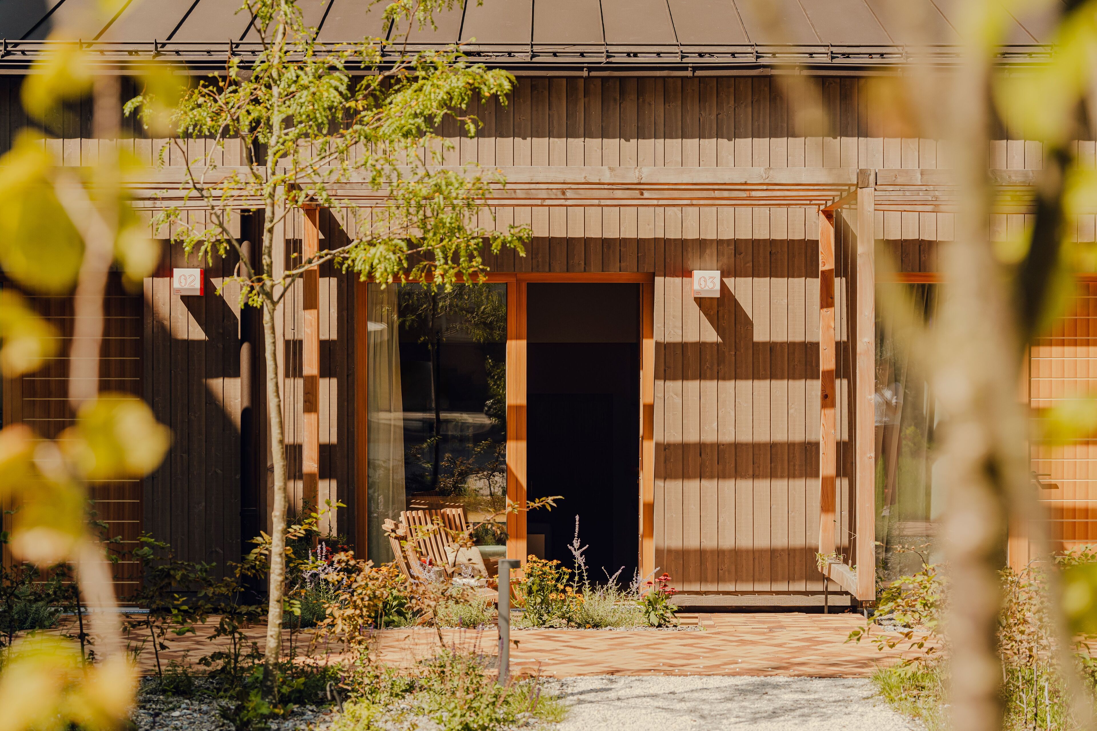 Un edificio de madera con un amplio acceso abierto, un pequeño espacio de estar al aire libre y una entrada pavimentada.