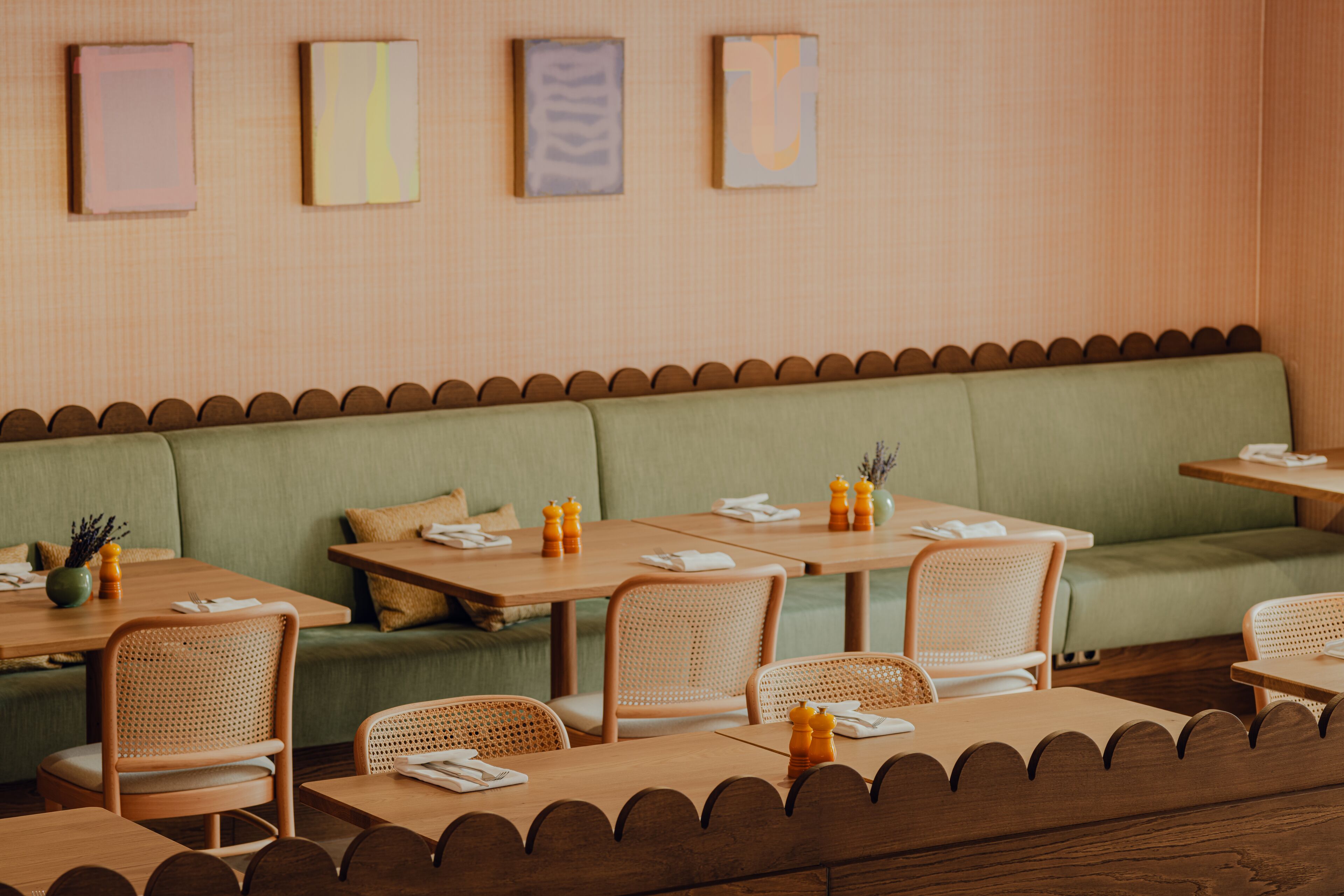 Un restaurante con mesas y sillas de madera, un banco con cojín verde y obras de arte en la pared.