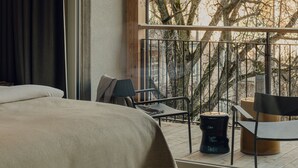 A bedroom with a large window, a bed, a chair, and a small table. - Design Hotel zum Hirschen Salzburg (Salzburg)