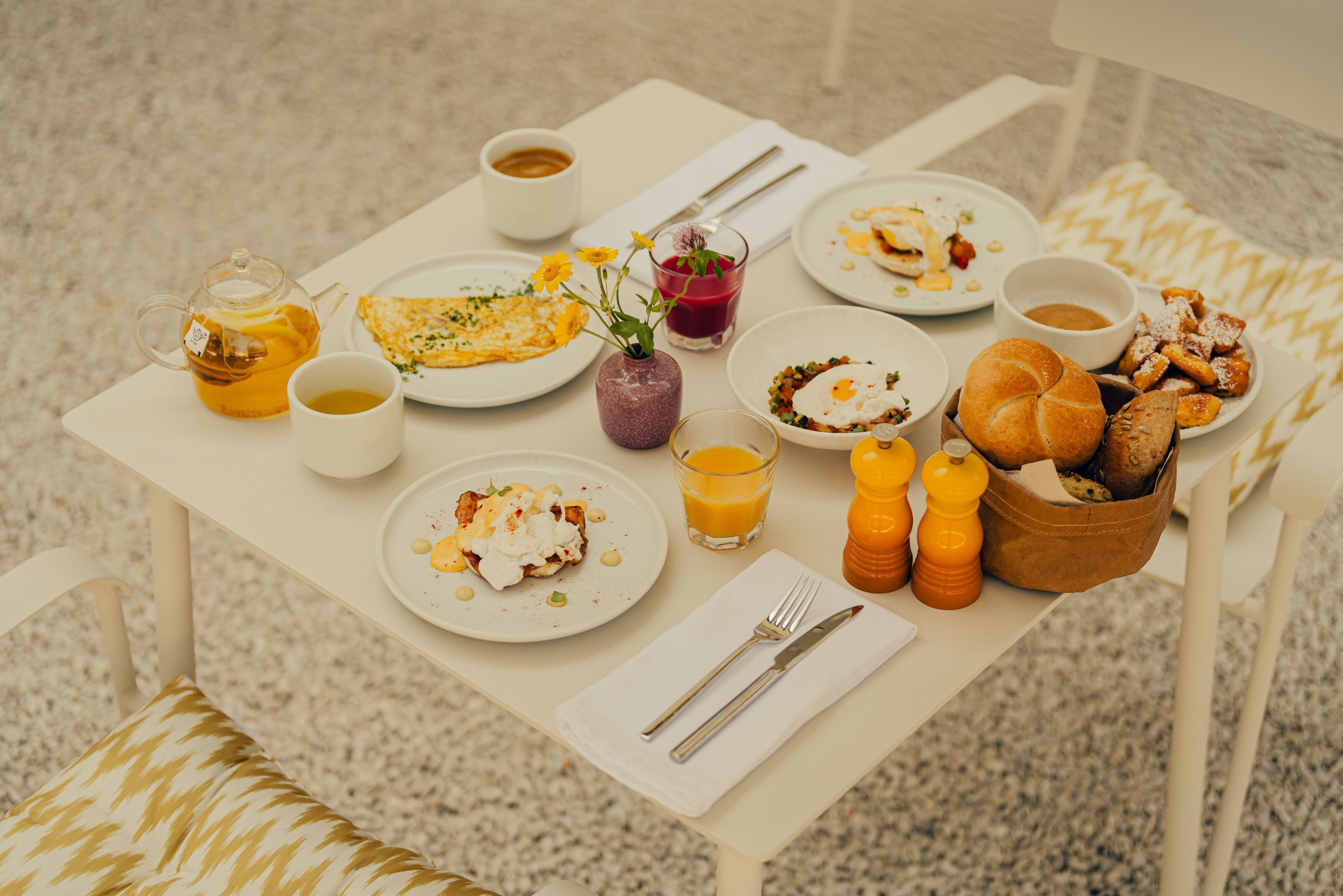 Et morgenbord med forskellige retter, en tepotte og en kop kaffe.