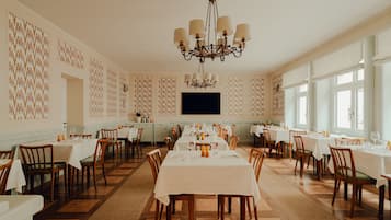 Un amplio comedor con varias mesas y sillas, una araña y papel tapiz estampado.