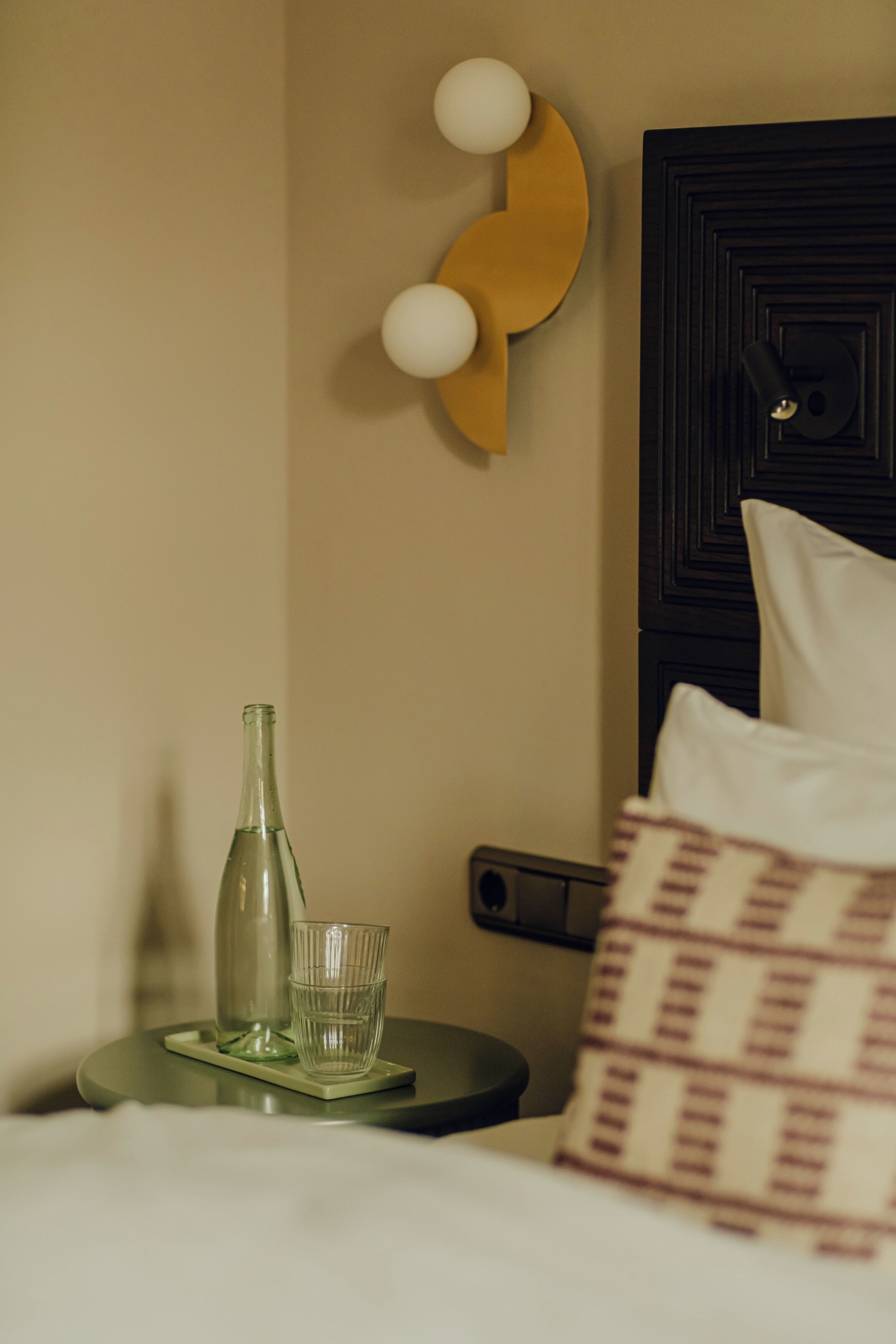Una cama bien hecha con una almohada, una mesita de noche con una botella y un vaso, y una decoración en la pared.