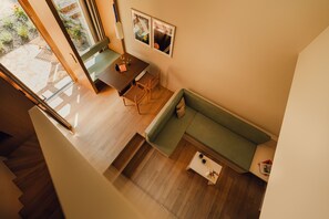 A modern interior with a wooden staircase, a green sofa, a dining table with chairs, and a small white table with items on it.