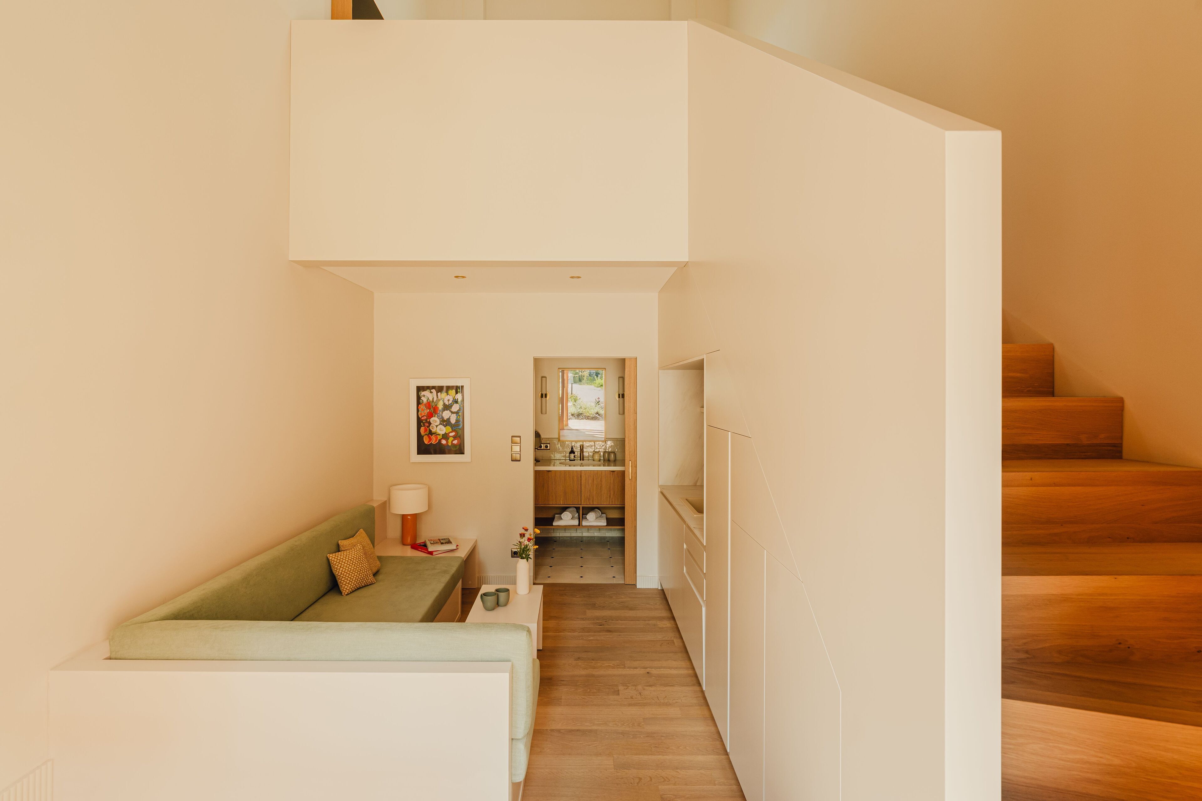 Un intérieur moderne avec un canapé vert, une petite table et un coin cuisine visible à travers une porte ouverte.