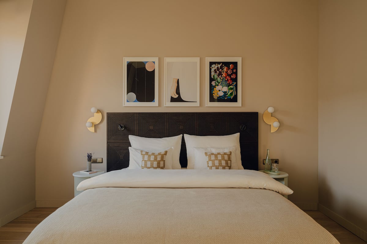 Un lit bien fait, avec une tête de lit, deux tables de chevet et trois œuvres d’art encadrées au-dessus du lit.
