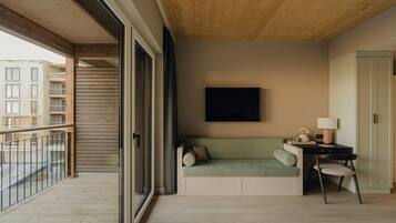 A modern room with a wooden ceiling, a green sofa, a desk with a chair, and a large window overlooking a building.