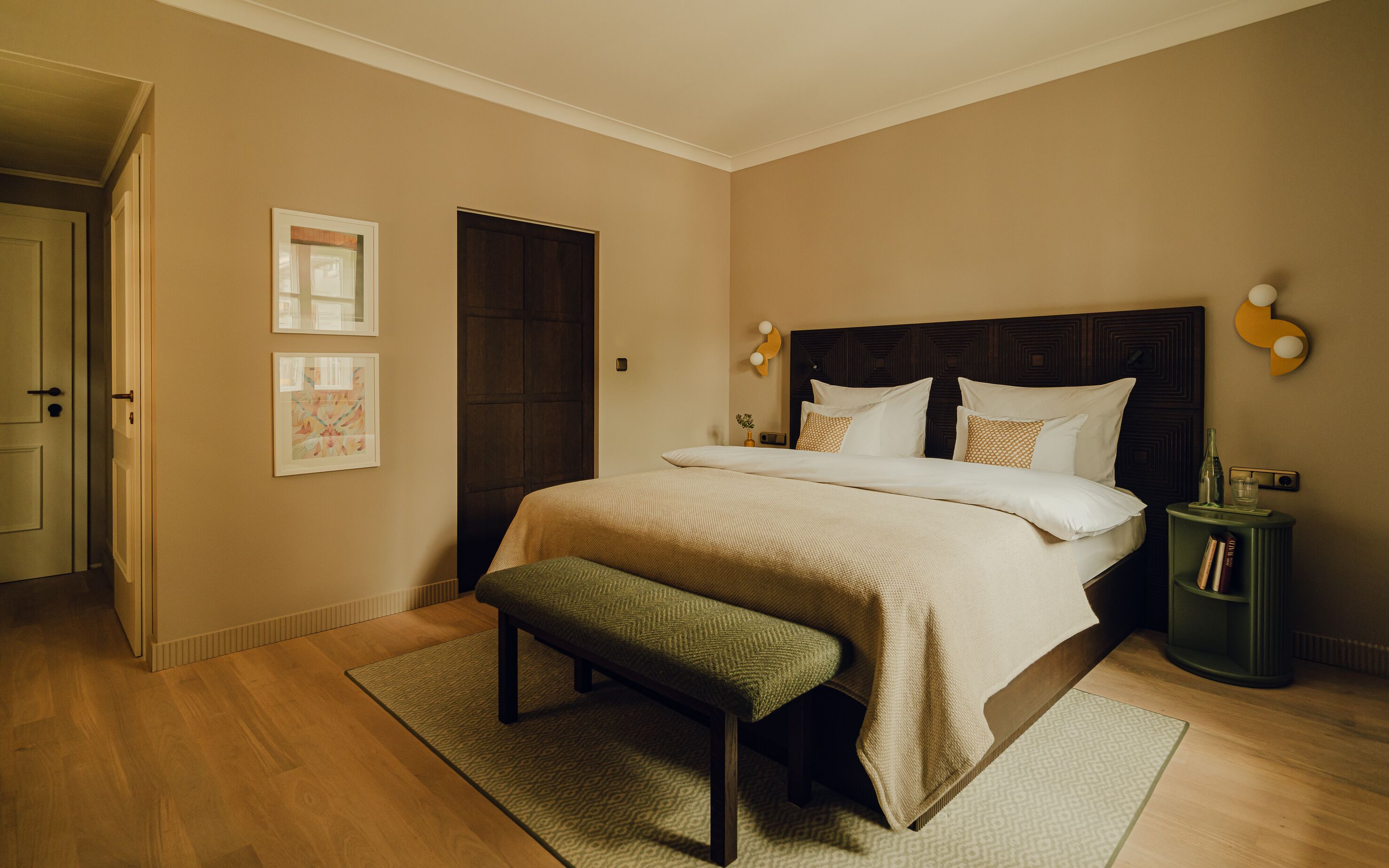 Un dormitorio con una cama grande, un banco, una mesita de noche y una puerta.