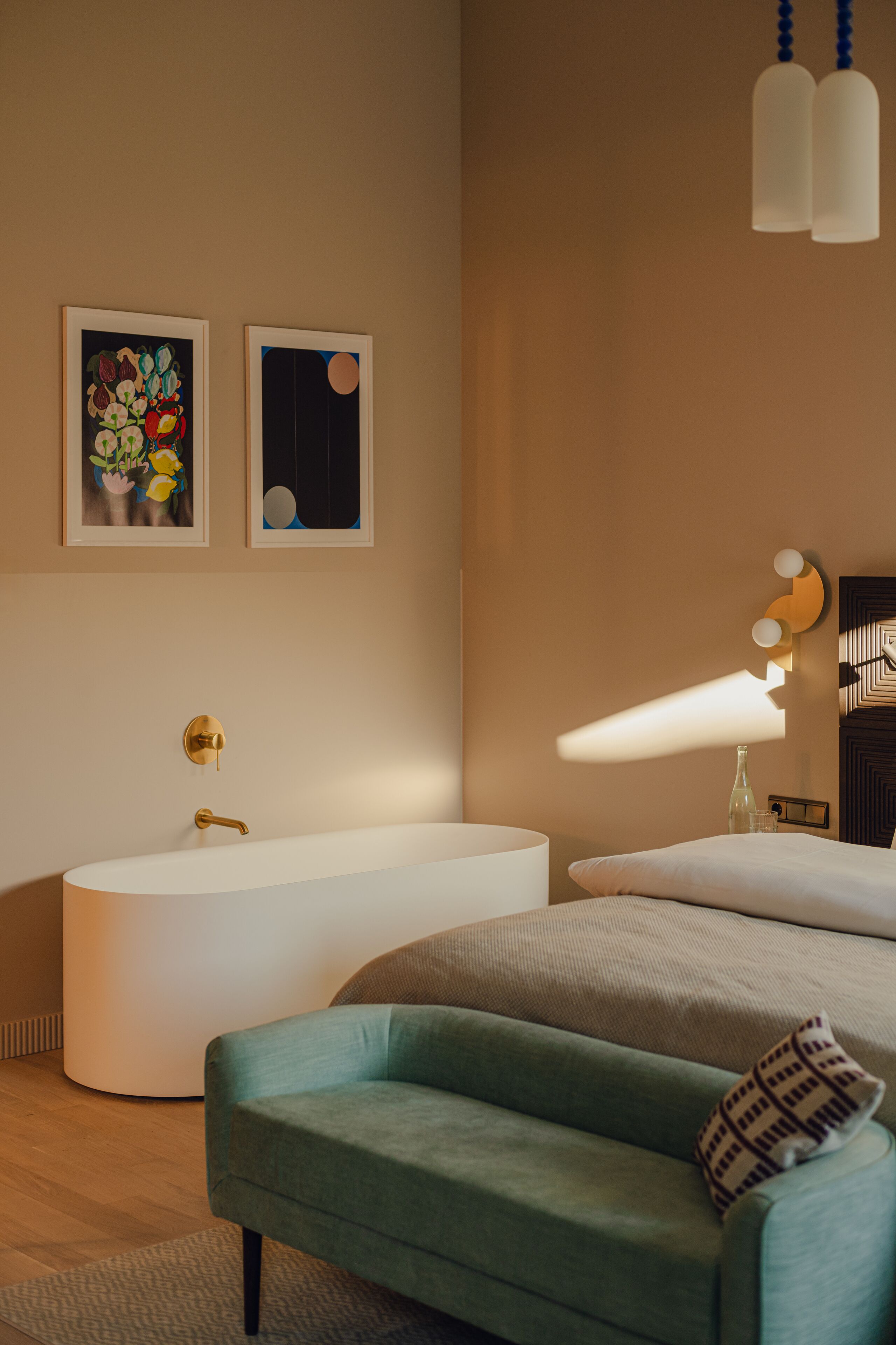 A modern bedroom with a large bed, a bathtub, and two framed artworks on the wall.