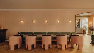 A restaurant interior with wooden flooring, green cushioned seating, and wall-mounted light fixtures.