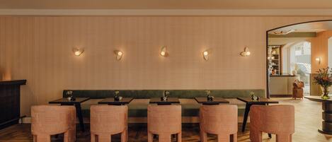 A restaurant interior with wooden flooring, green cushioned seating, and wall-mounted light fixtures.