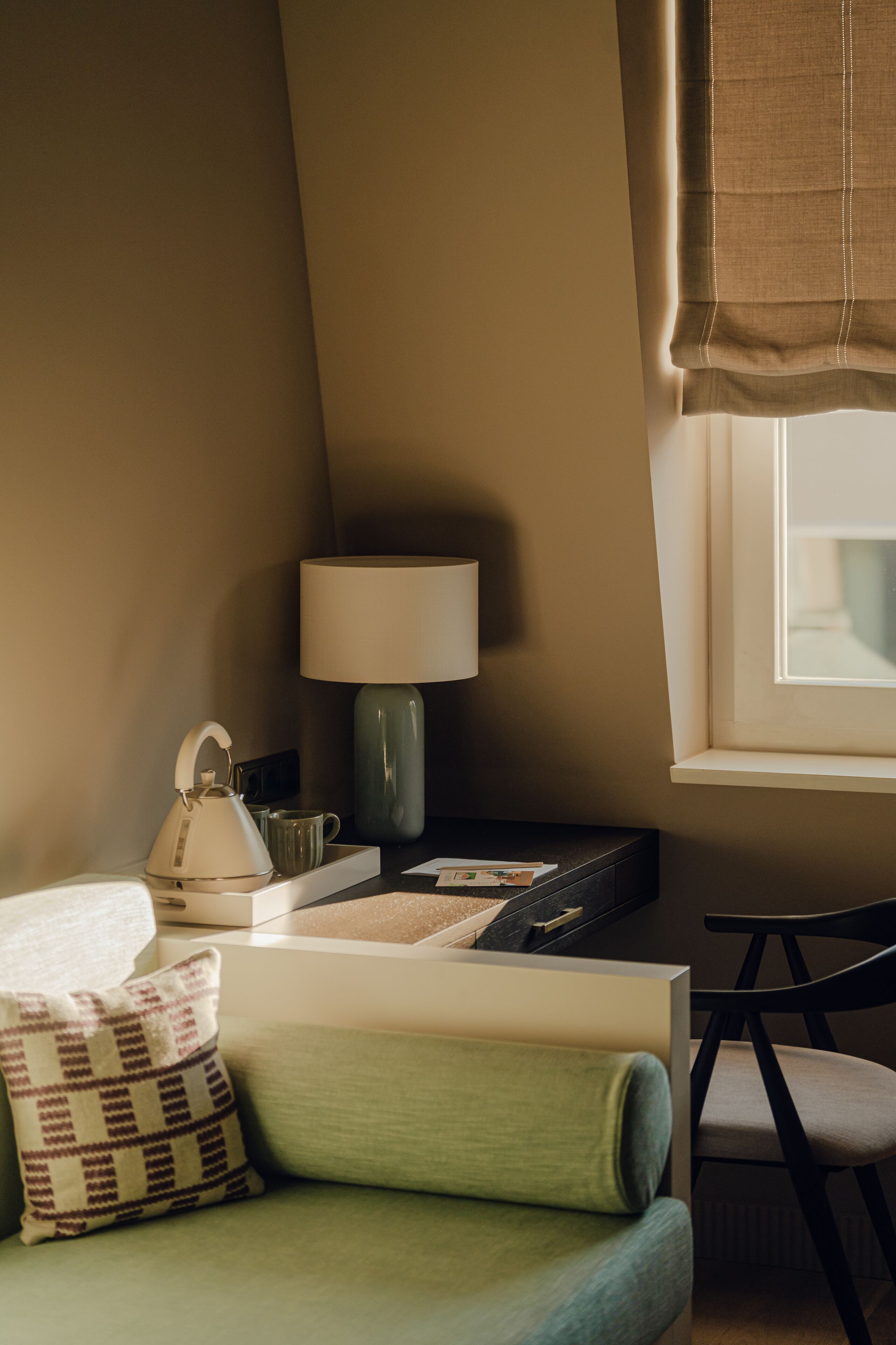 Ein gemütliches Zimmer mit einem grünen Sofa, einer Lampe, einem Wasserkocher und einem Fenster mit Vorhängen.