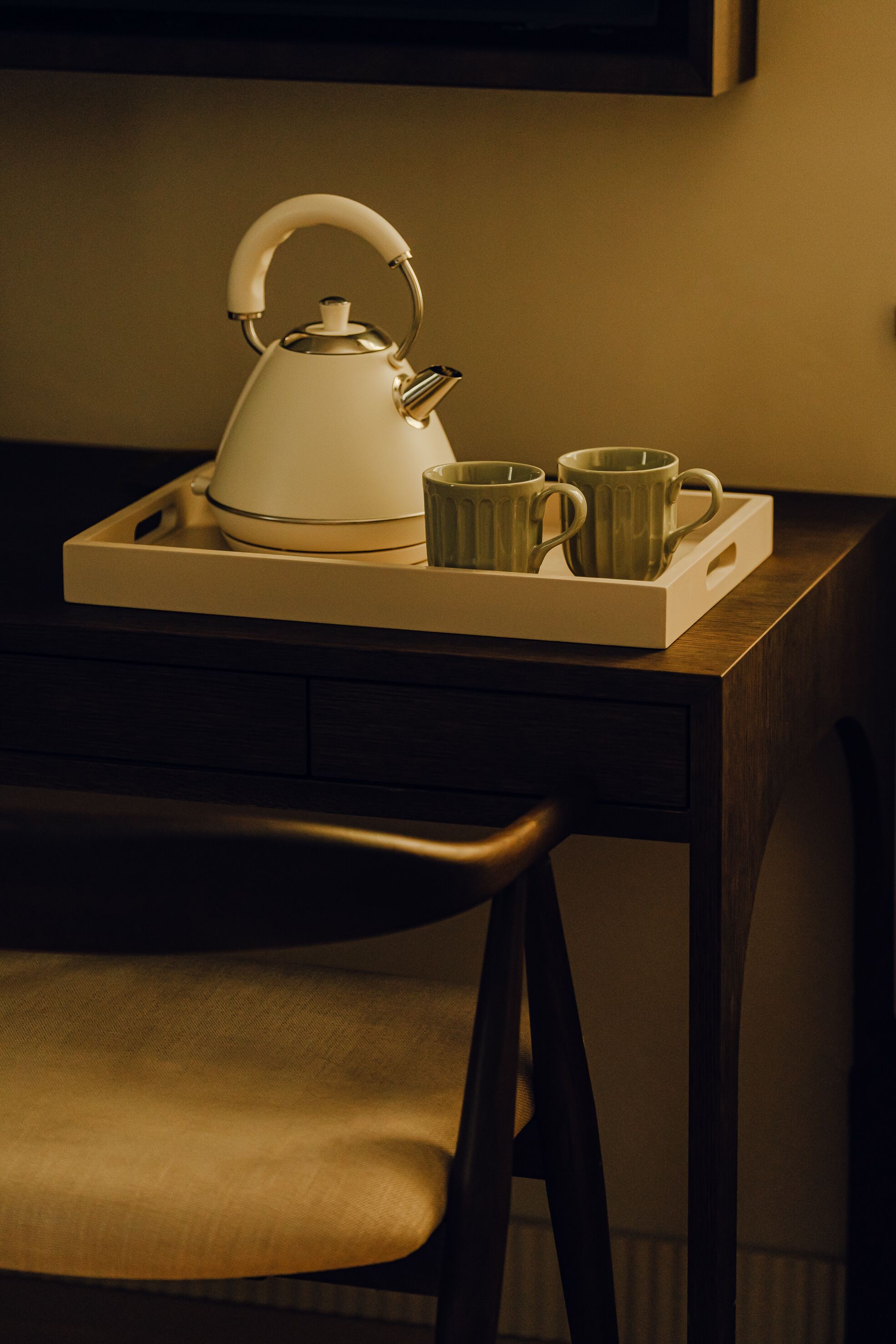 A tray with a kettle and three mugs on a wooden table.
