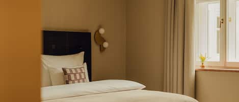 Una cama bien hecha con cabecera, mesita de noche y una ventana con cortinas.
