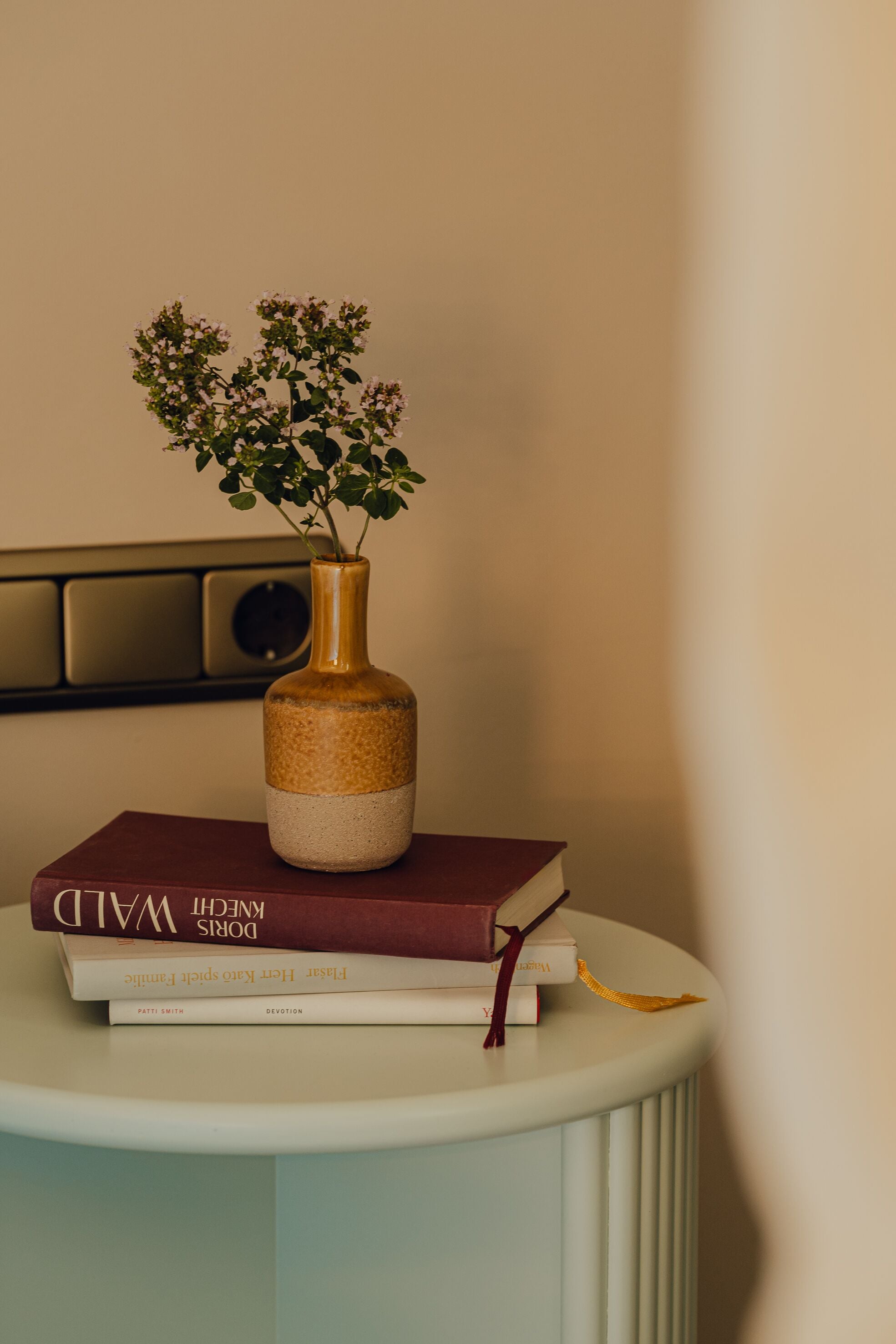 A white pedestal table with a vase containing a plant and a stack of books.
