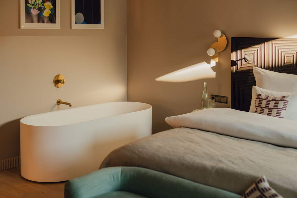 Une chambre à coucher moderne avec une grande baignoire, un lit doté d’une tête de lit à motifs et des luminaires fixés au mur.