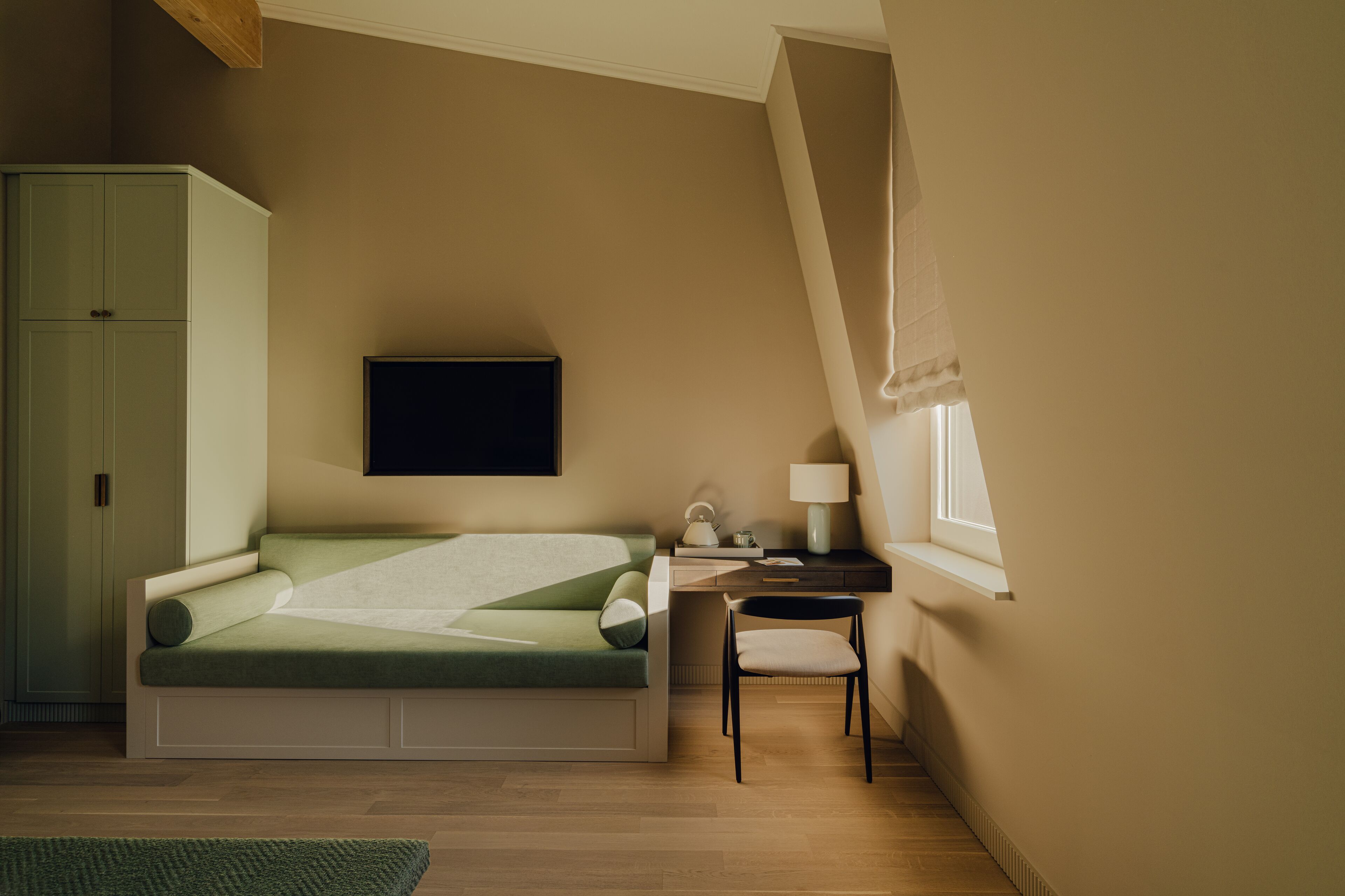 A bedroom with a bed, a desk, a chair, a television, and a window.