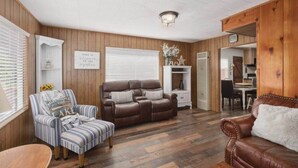 Ein gemütliches Wohnzimmer mit einem braunen Ledersofa, einem gestreiften Sessel und Holzboden.