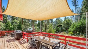Eine Holzterrasse mit roter Geländer, einem Tisch mit Stühlen und einem überdachten Grill.