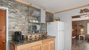 Eine Küche mit Steinrückwand, Holdekor-Schränken, einem weißen Kühlschrank und einer Kaffeemaschine auf der Arbeitsplatte.