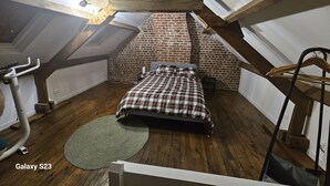 Slaapkamer in loftstijl met bakstenen muur, houten balken, een bed, loopband en een hangende kledingrek.