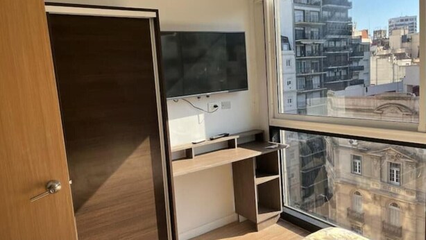 Ein Schlafzimmer mit Bett, Fernseher, Schreibtisch und einem Fenster mit Blick auf die Stadt.