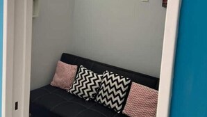 Ein Zimmer mit einer schwarzen Couch, zwei gemusterten Kissen, einem Deckenventilator und einer Leuchte.