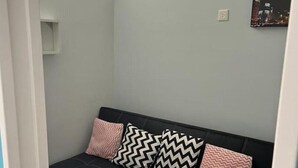 Ein Zimmer mit einer schwarzen Couch, einer hellblauen Wand, einem kleinen weißen Regal und einem gerahmten Bild.