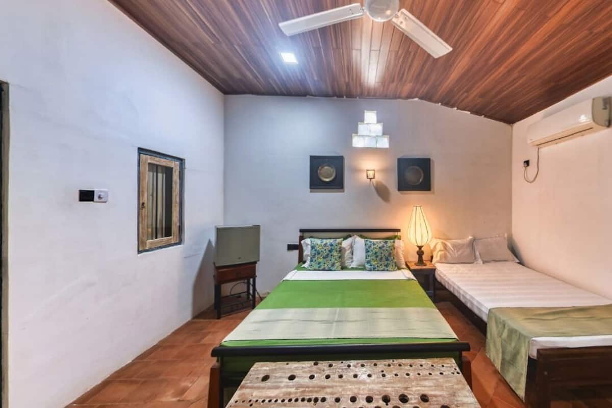 Una habitación pequeña y acogedora con dos camas individuales, techo de madera y colcha verde.