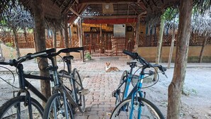 A covered outdoor area with bicycles parked under a wooden structure, a dog lying on the ground, and a brick pathway. - Wild Wadi wilpattu (Eluwankulama)