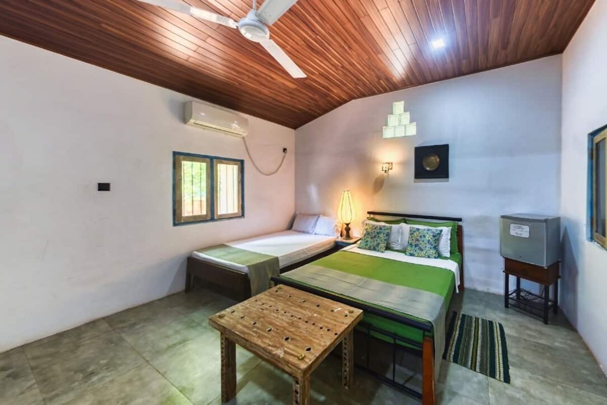 Una habitación pequeña y acogedora con techo de madera, una cama con ropa de cama verde, una mesita de noche, una pequeña mesa y un televisor sobre un mueble.