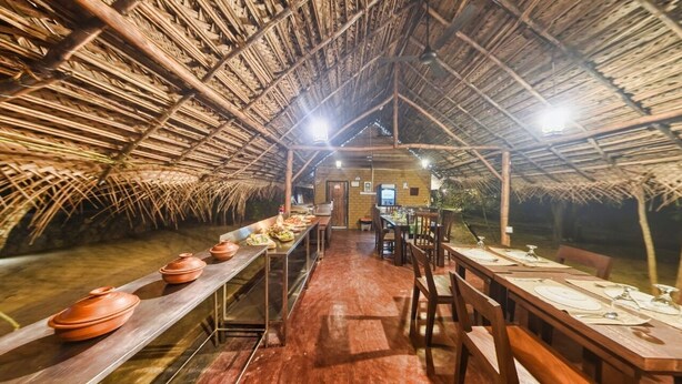 Un espace de restauration doté d’un toit de chaume et de longues tables en bois, préparé pour un repas.