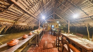 A thatched-roof dining area with long wooden tables set for a meal.