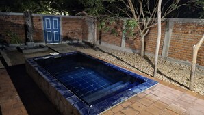 Une piscine rectangulaire aux parois recouvertes de carreaux bleus, entourée d’un mur de briques et d’une zone recouverte de gravier.