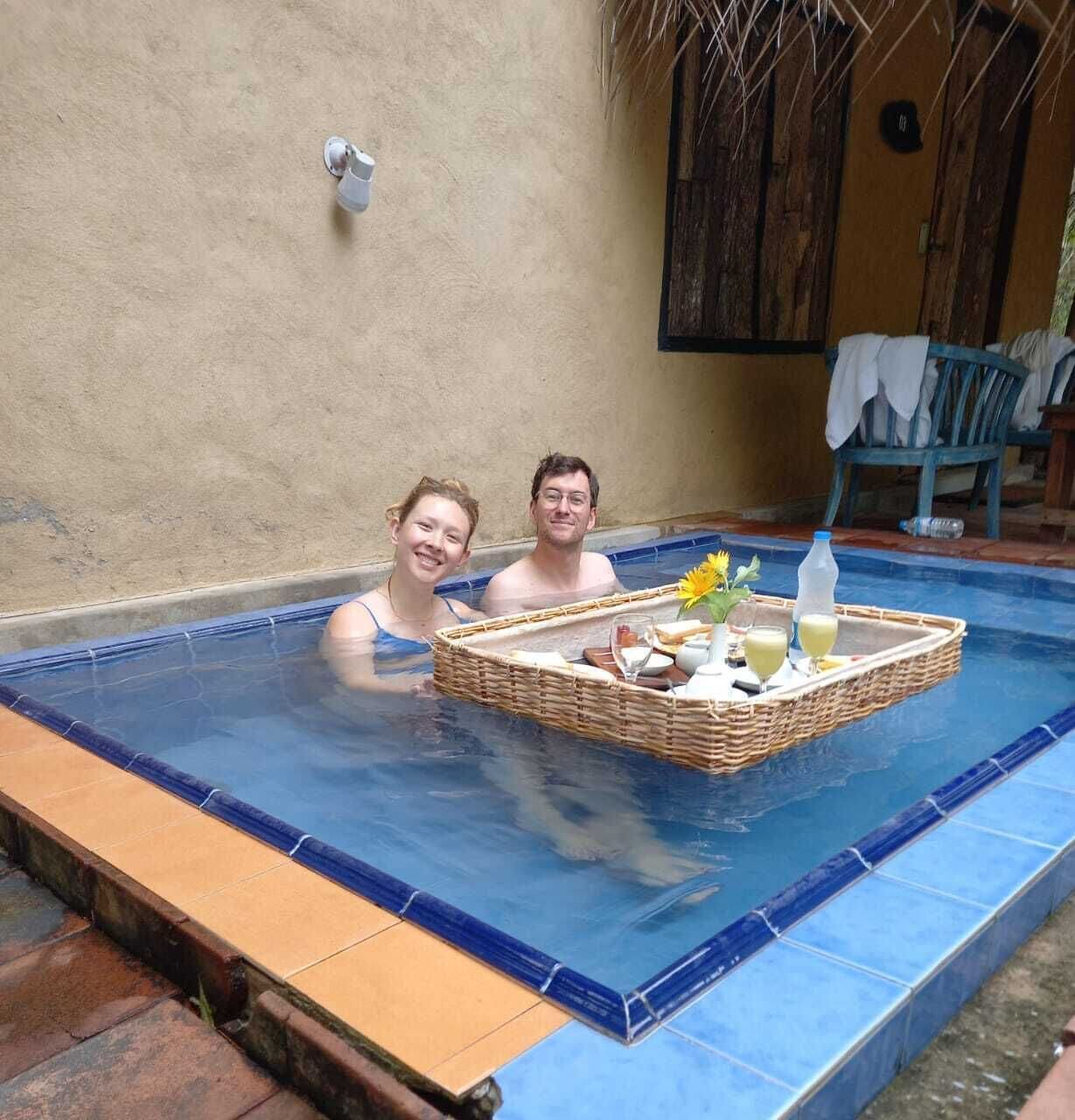Una piscina pequeña al aire libre con una bandeja de mimbre que contiene una flor, una botella y un vaso.