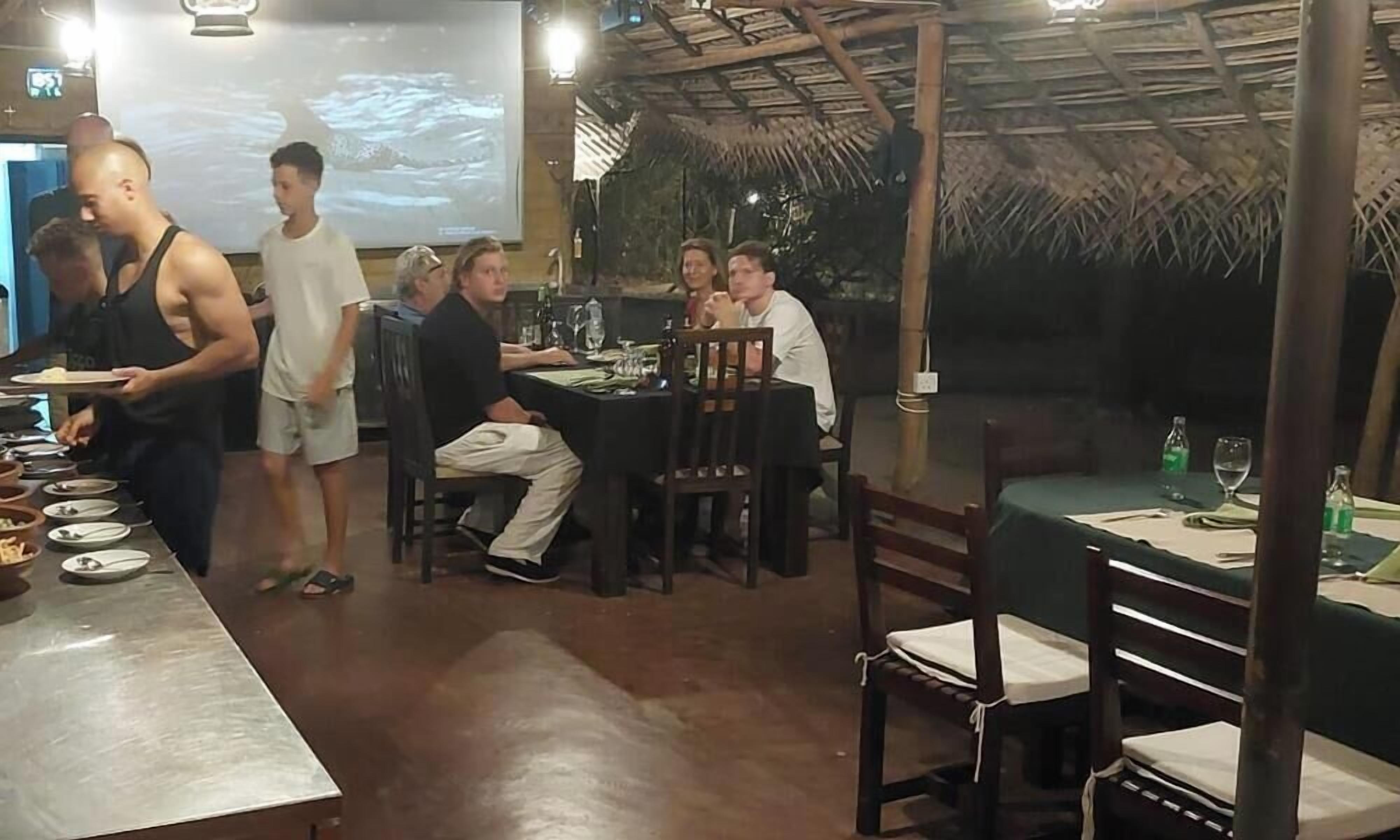 Un restaurant doté d’un toit de chaume, de tables et de chaises en bois.