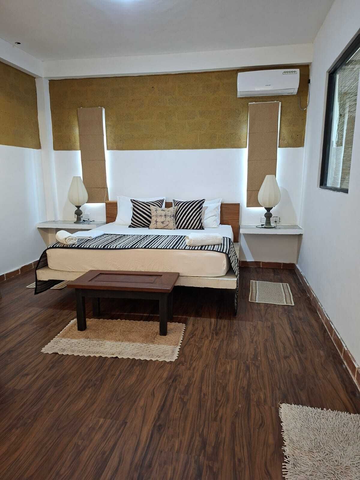 A hotel room with a bed, bedside tables, a nightstand, a wooden coffee table, and a window.