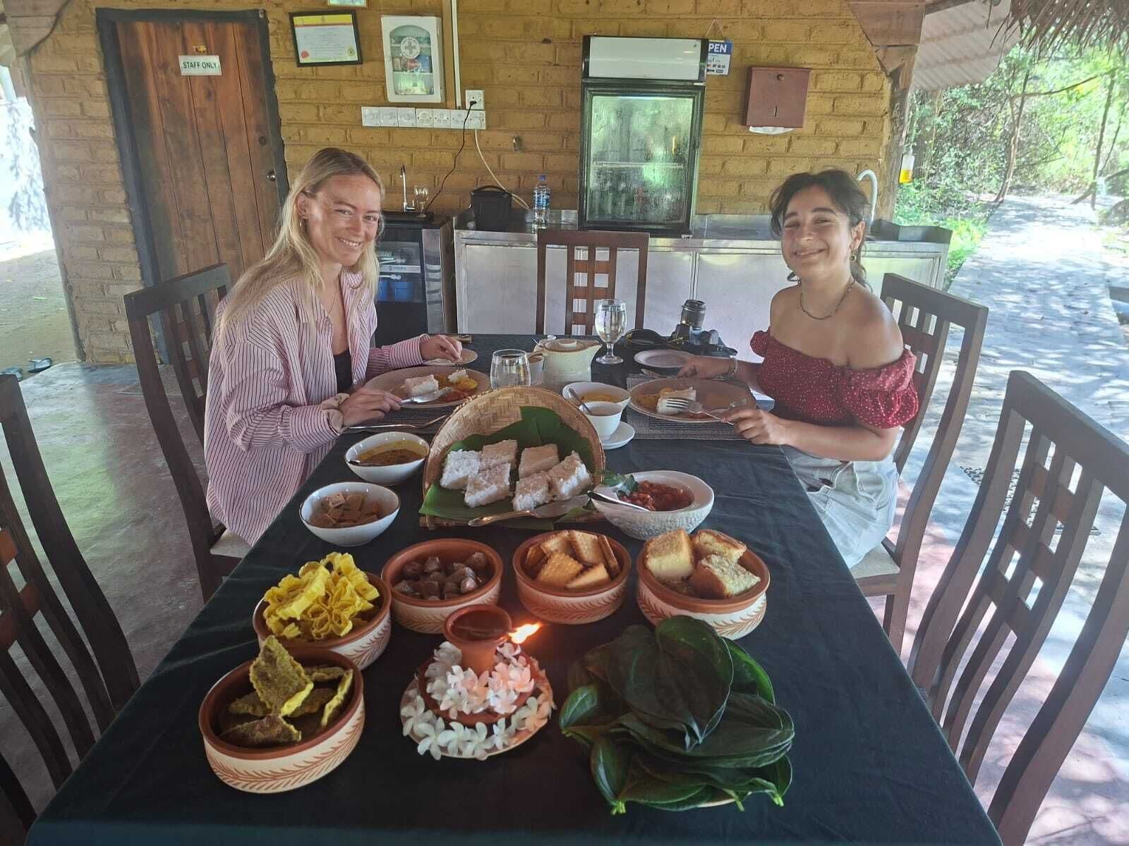 Dos personas cenando en una mesa con varios platos, una pequeña zona de cocina y una puerta con la inscripción 'STAFF ONLY' al fondo.