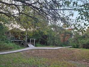 A garden with a concrete pathway leading to a white structure, surrounded by dense foliage and a building in the background. - Wild Wadi wilpattu  (Eluwankulama)